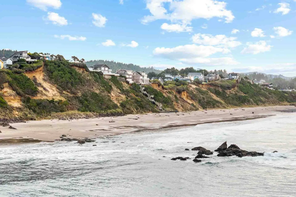 A panoramic coastal view featuring sandy beaches, gentle ocean waves, rock formations, and cliffside homes. The setting is ideal for activities like beachcombing, kite flying, and long family walks by the water.