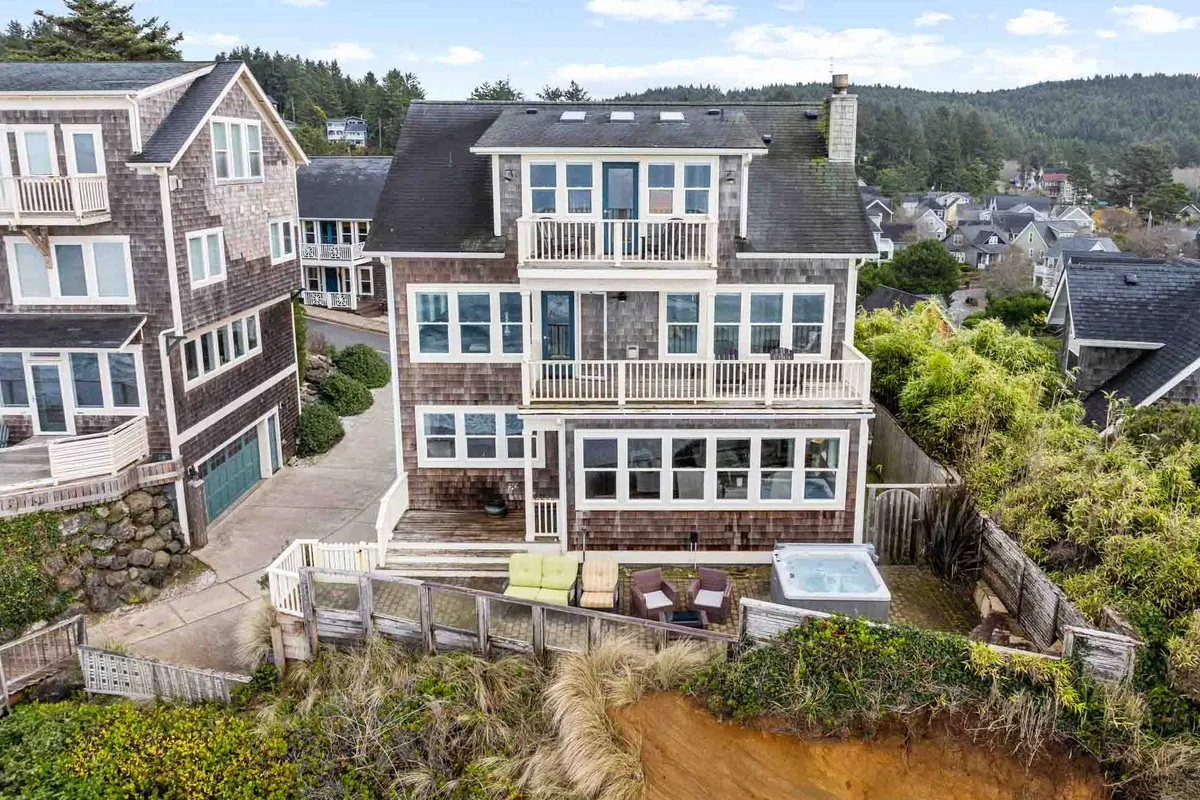 This exterior shot showcases the home's large windows, a hot tub on the deck, balcony seating, and landscaped gardens. The setting is ideal for group gatherings and outdoor relaxation, with ample space for entertaining and enjoying the natural surroundings.