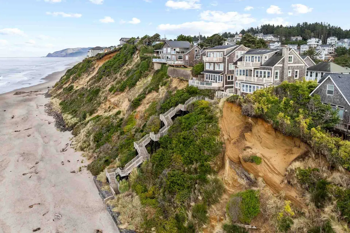 An exterior shot of cliffside homes with a staircase leading down to the sandy beach, overlooking the ocean and coastal vegetation. The image suggests easy access to the beach and the natural beauty surrounding the area.
