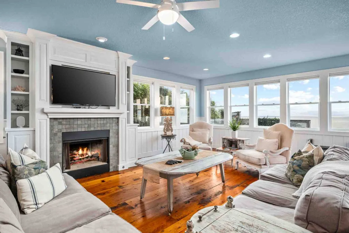 A warm and welcoming living area featuring a modern gas fireplace, large windows, and plush seating. A decorative table anchors the space, while sunlight pours in, creating an inviting atmosphere perfect for gatherings or quiet evenings by the fire.