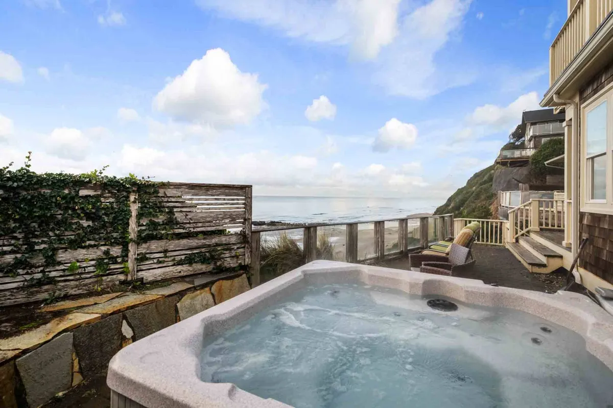 This image captures a serene wooden deck with a hot tub overlooking the ocean, set beneath a cloudy sky. The inviting hot tub and comfortable deck seating set the stage for relaxation and romantic moments, perfectly showcasing the luxury coastal retreat experience.