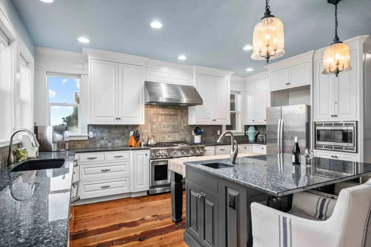 A stylish kitchen with a prominent granite island, high-end stainless steel appliances, white cabinetry, and elegant hanging pendant lights. The space looks inviting for both cooking and entertaining, with ample room for family or friends to gather around.