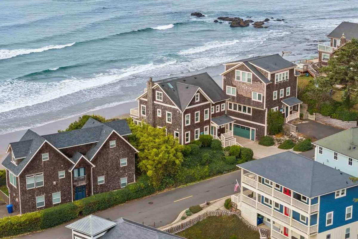 A peaceful scene of ocean waves rolling onto a sandy beach, bordered by coastal homes and greenery. The setting is perfect for family gatherings, water sports, or simply relaxing while watching the sunset.