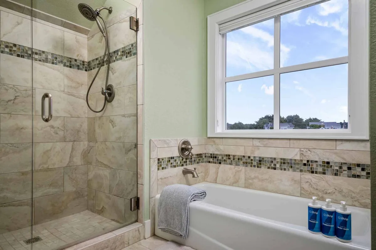 A spa-like bathroom with a glass shower enclosure, a soaking tub, and a window that lets in gentle sunlight. The tranquil mood is accentuated by the modern, clean lines and the inviting bath features.
